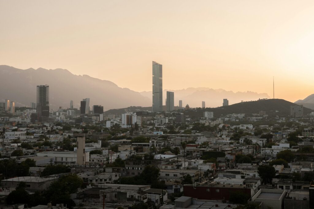 Aerial view of Monterrey's skyline at sunset, featuring modern skyscrapers and mountains.